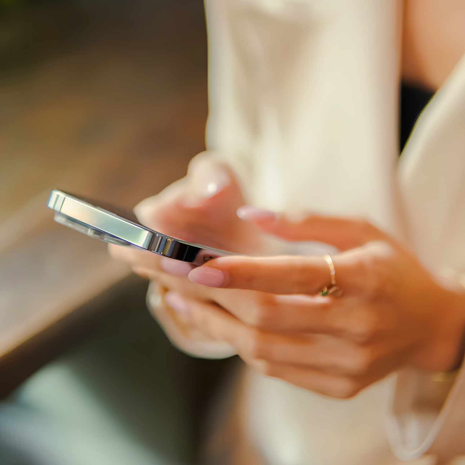 Hands holding a phone with polished nails and a gold ring