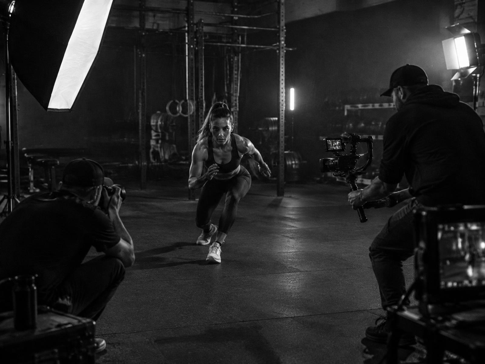 Fitness athlete mid-shoot with a camera crew in a dark gym